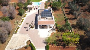 An aerial view of a house with a solar panel roof, a swimming pool, and a well-maintained garden.