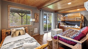 A cozy room with a wooden ceiling, a large bed with a checkered blanket, a bunk bed, and a window with blinds. - Rustic A-Frame Cabin | Dock | Paddleboards | Summer Camp Vibes (Coeur D'Alene)