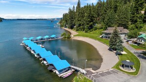 An aerial view of a lakeside property with a dock, a covered boat launch area, and a small pavilion. - Rustic A-Frame Cabin | Dock | Paddleboards | Summer Camp Vibes (Coeur D'Alene)