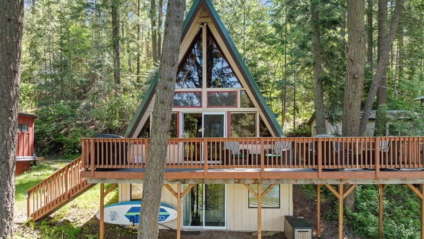 A cabin with a wooden deck, a glass door, and a small attached shed. - Rustic A-Frame Cabin | Dock | Paddleboards | Summer Camp Vibes (Coeur D'Alene)