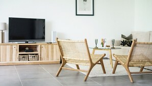 A modern living room with a flat-screen TV, wicker chairs, a glass coffee table, and a framed picture on the wall. - Le Prince D'orion in the heart of the island for families and professionals (Fort-de-France)