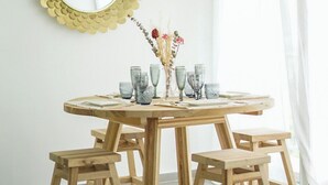 A round wooden dining table with four stools, a gold-framed mirror, and a vase with dried flowers on the wall. - Le Prince D'orion in the heart of the island for families and professionals (Fort-de-France)