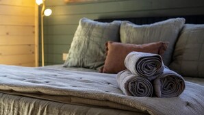 A bed with a rolled-up blanket and pillows, a floor lamp, and a window with daylight. - Artisan's Retreat — Rooftop Hot Tub & Free Tickets (Gatlinburg)