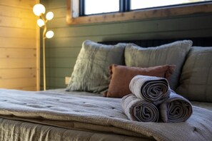 A bed with a rolled-up blanket and pillows, a floor lamp, and a window with daylight. - Artisan's Retreat — Rooftop Hot Tub & Free Tickets (Gatlinburg)