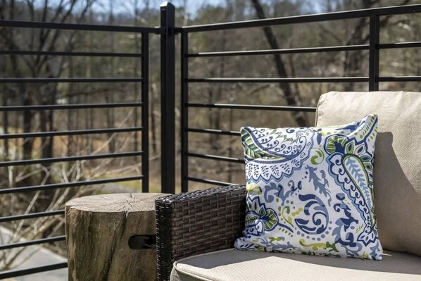 A wicker chair with a cushion and a patterned pillow on a balcony with a metal railing.