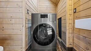 A compact, modern, stainless steel front-loading washer and dryer unit installed in a wooden cabin with a sloped ceiling. - Artisan's Retreat — Rooftop Hot Tub & Free Tickets (Gatlinburg)