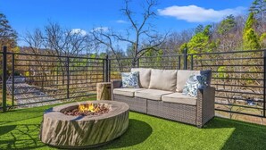 A patio area with a fire pit, a wicker sofa with cushions, and a metal fence. - Artisan's Retreat — Rooftop Hot Tub & Free Tickets (Gatlinburg)