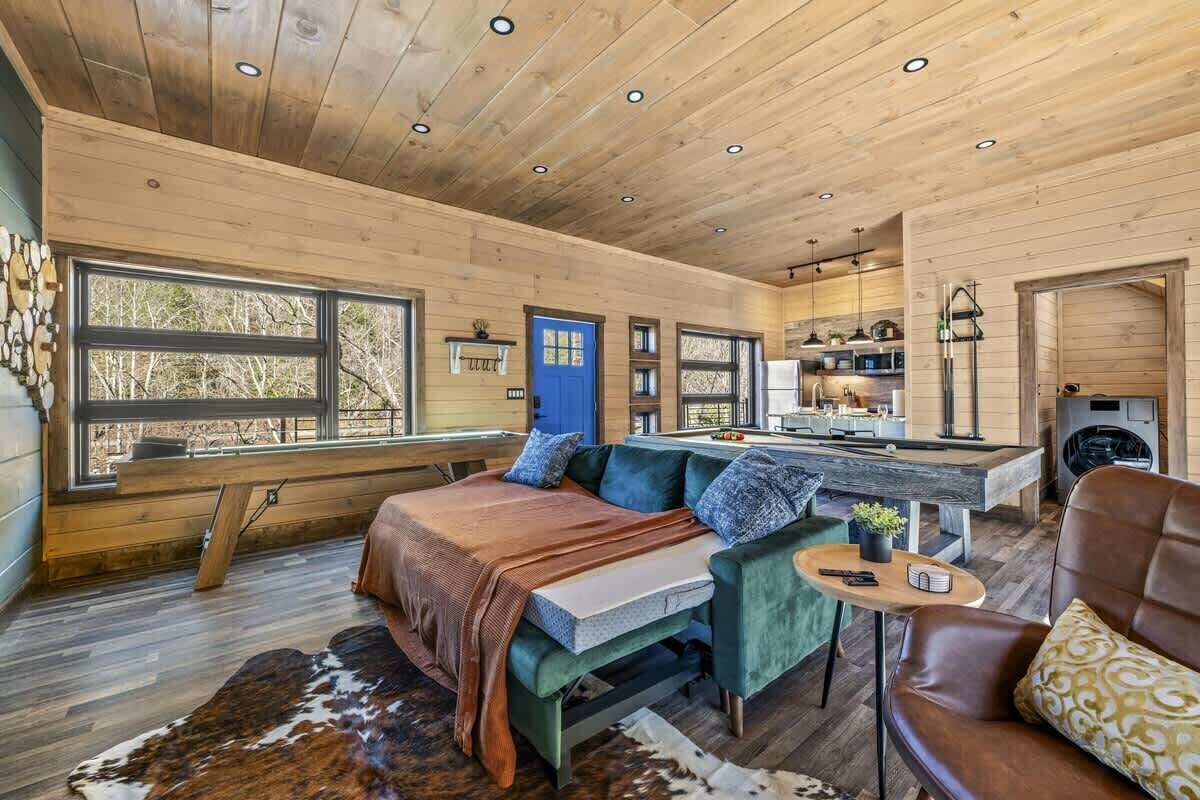 A cozy cabin interior with a large bed, seating area, kitchen, and a view of the outdoors.