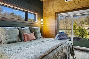 Una camera da letto con un letto grande, diversi cuscini, un comodino e una finestra vista alberi.
