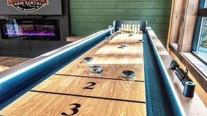 Een jeu de boules tafel met genummerde scorezones, een open haard en een raam met uitzicht.