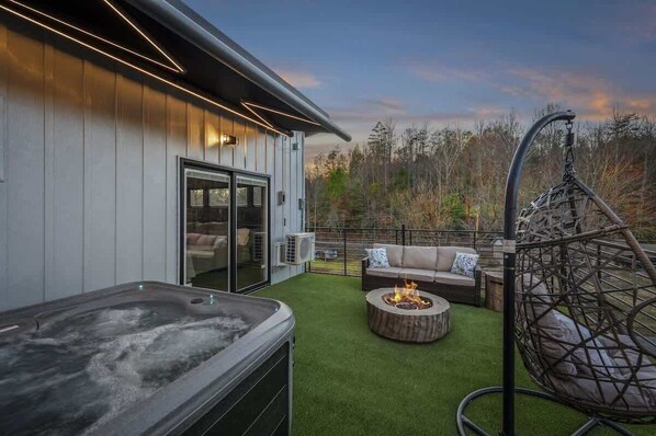 Une terrasse extérieure avec un jacuzzi, un foyer et un fauteuil suspendu.