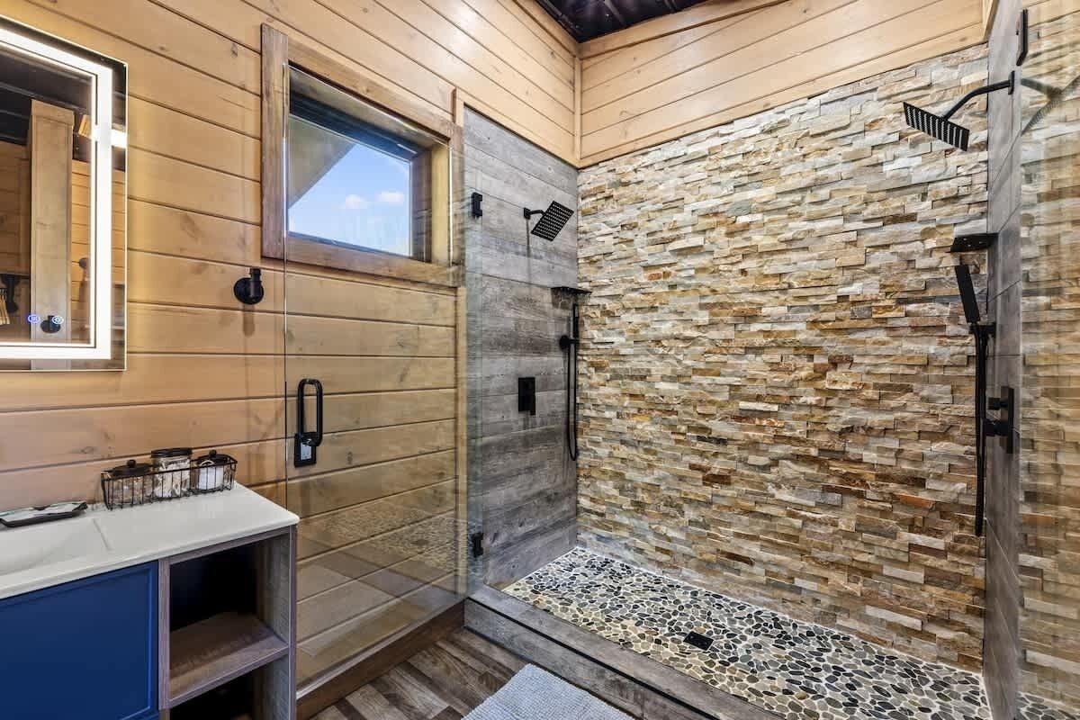 A bathroom with wooden walls, a stone wall shower, and a window.