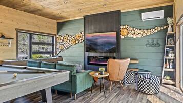 A pool table with a sofa and chairs, a fireplace, and a wall decorated with wooden circles.