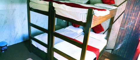 A bunk bed with white bedding and red pillows, a wooden headboard, and a small rug on the floor.