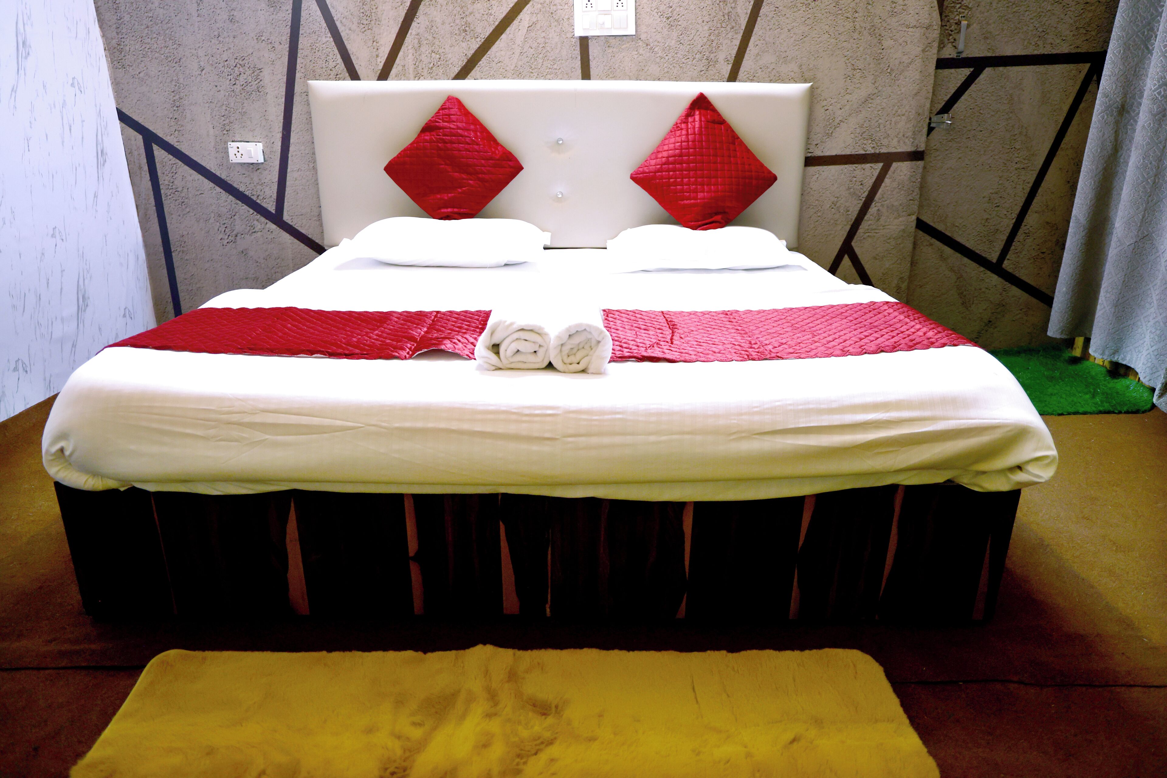 A neatly made bed with a white and red bedspread, two red pillows, and two rolled towels on the bed.