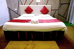 A neatly made bed with a white and red bedspread, two red pillows, and two rolled towels on the bed.