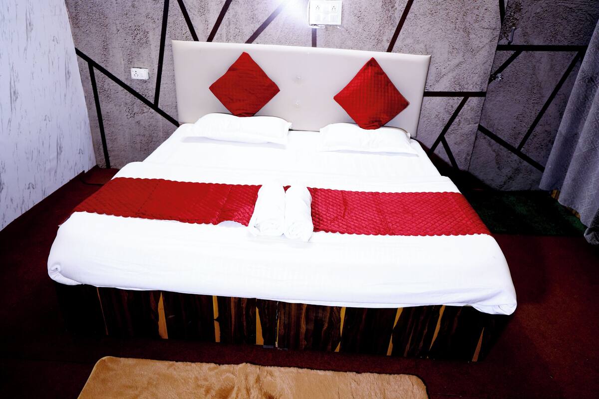 Uma cama com edredom branco e vermelho, cabeceira de madeira e almofadas vermelhas.