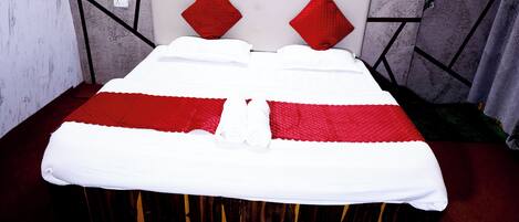 A bed with a white and red bedspread, a wooden headboard, and red pillows.