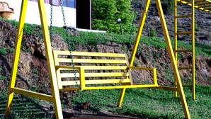 A yellow swing set in a grassy area with a house in the background. - The Escapee Resort (Dhanaulti)