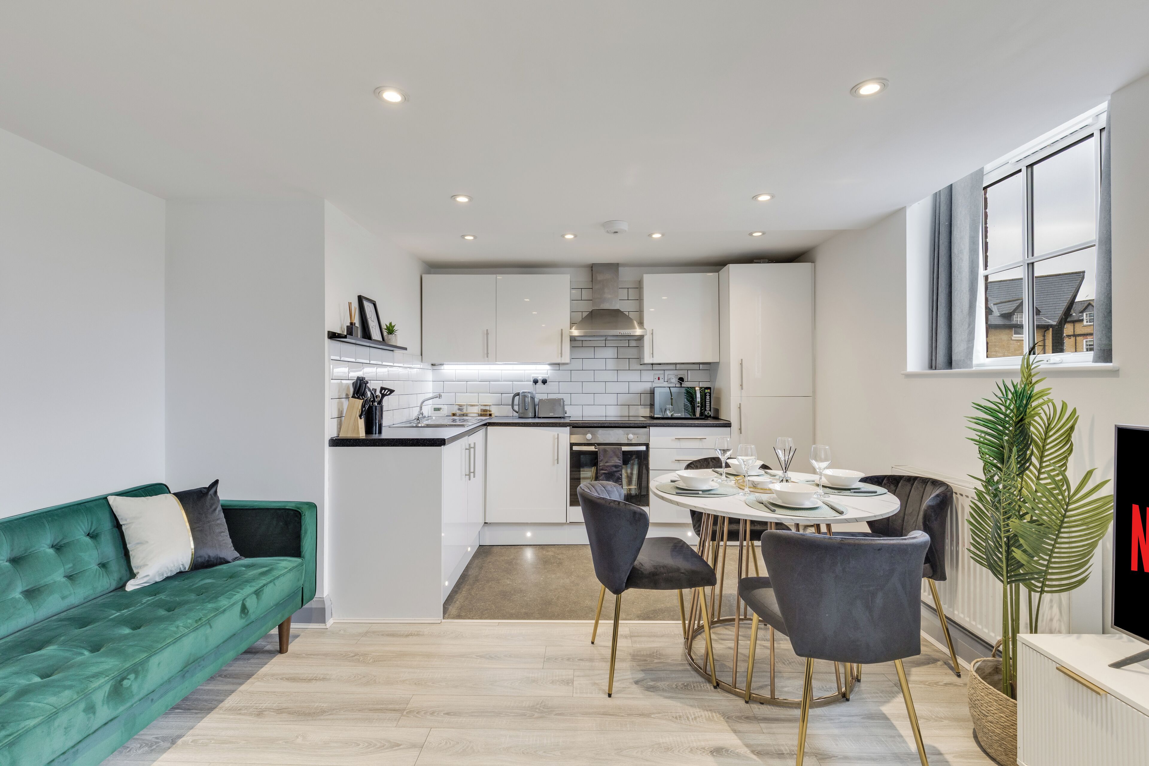 A modern kitchen with white cabinets, a dining area with a round table and chairs, and a green sofa.