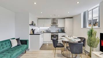 A modern kitchen with white cabinets, a dining area with a round table and chairs, and a green sofa.