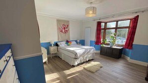 Un dormitorio con cama, mesitas de noche, lámpara colgante, ventana con cortinas y vistas al exterior.