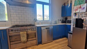 Una cocina con gabinetes azules, estufa de acero inoxidable, lavavajillas y refrigerador con imanes y mensajes.