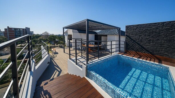 A rooftop pool area with a modern pool, a wooden deck, and a white building with a black roof. - Residence del Maestro Apartments (Asunción)