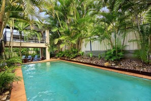 A swimming pool surrounded by lush greenery, a covered outdoor seating area, and a multi-level structure. - 5BR Coastal Escape, Walk to Peregian Beach! (Peregian Beach)
