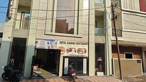 Un immeuble à plusieurs étages, sur lequel on peut lire l’enseigne « Hôtel Gaurav Restaurant », indiquant qu’il propose des chambres de qualité supérieure, des chambres de luxe et des chambres confortables.