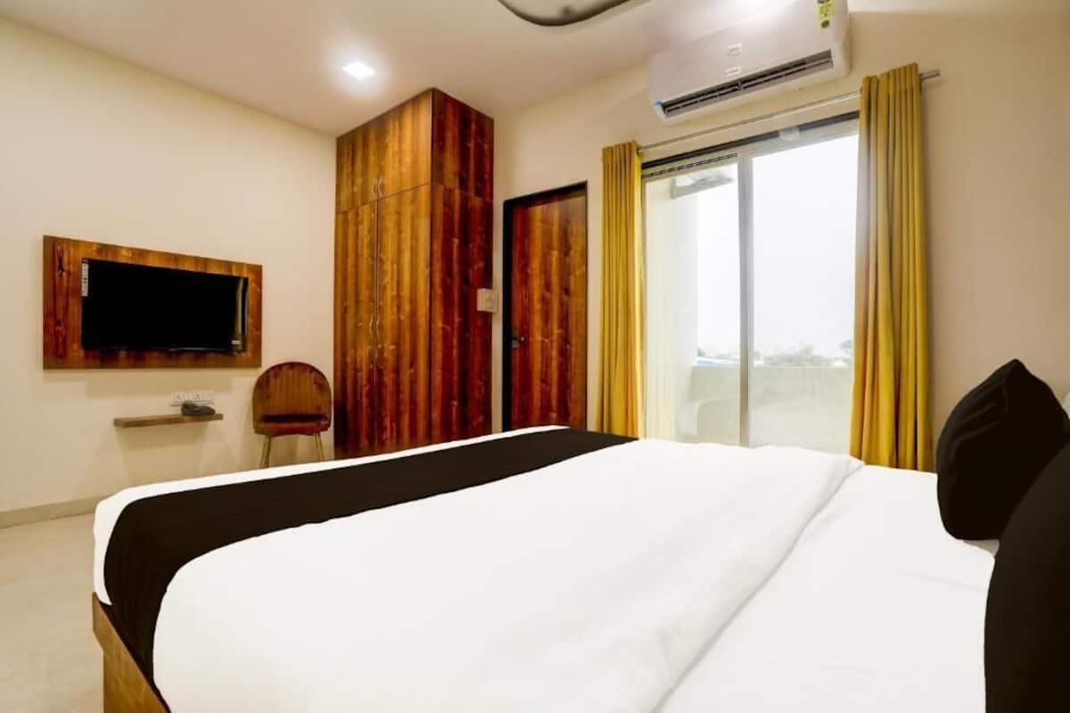 A hotel room with a bed, a television mounted on the wall, a wardrobe, and a window with curtains.