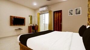 Une chambre d’hôtel dotée d’un grand lit, d’un téléviseur à écran plat fixé au mur, d’un climatiseur, d’un bureau avec une chaise et de deux tableaux encadrés accrochés au mur.
