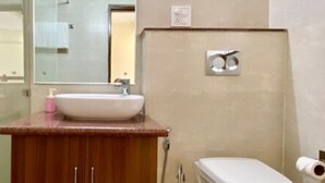 Un baño con tocador de madera, lavamanos, espejo, inodoro y ducha.