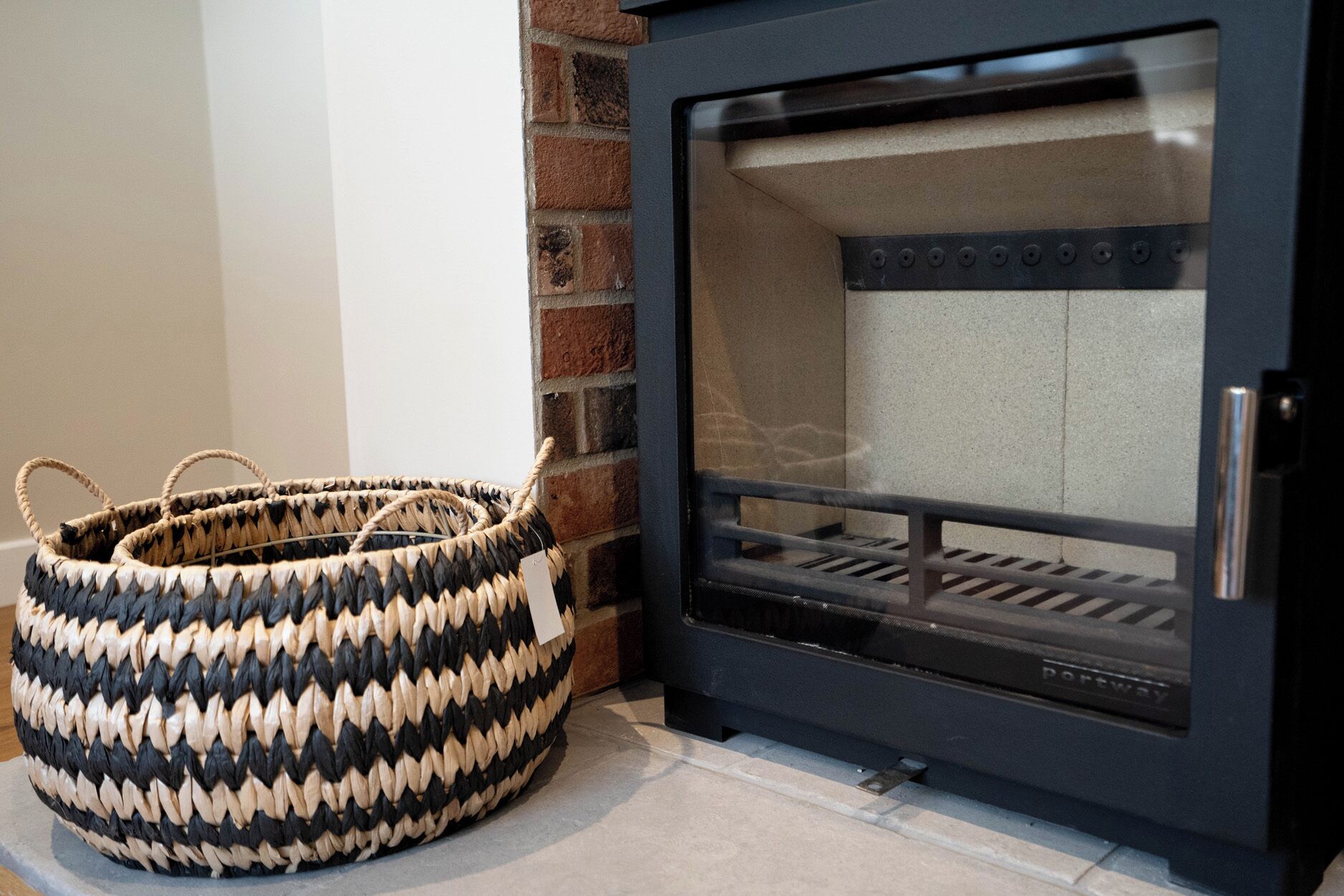 A fireplace with a glass door, a woven basket, and a brick wall.