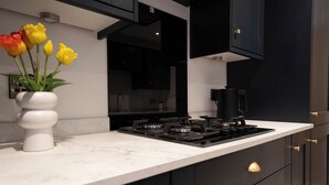 A modern kitchen with a marble countertop, black cabinets, and a gas stove. - The Cove (Lowestoft)