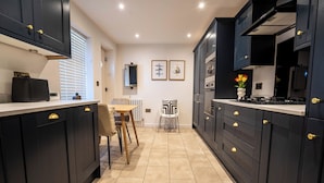 A modern kitchen with dark cabinetry, a central island, and a dining area with chairs. - The Cove (Lowestoft)