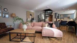 A modern living room with a pink sofa, a wooden coffee table, and a staircase leading to a kitchen. - Coral Cottage (Lowestoft)