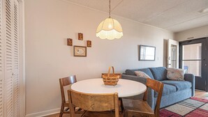 A dining area with a round table, wooden chairs, a hanging light fixture, a blue sofa, and a patterned rug.