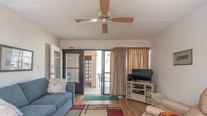 A living room with a ceiling fan, a sofa, a television, and a wooden chair.