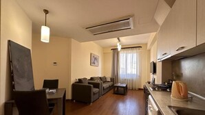 A compact living space with a dining area, sofa set, kitchenette, and a ceiling-mounted air conditioner.