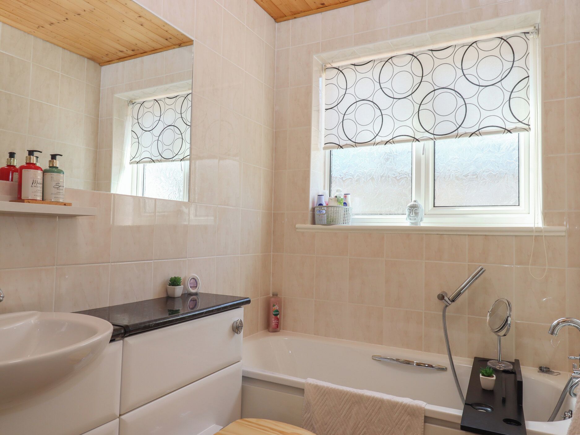 Une salle de bain moderne avec une baignoire, un lavabo et une fenêtre ornée d’un motif circulaire.