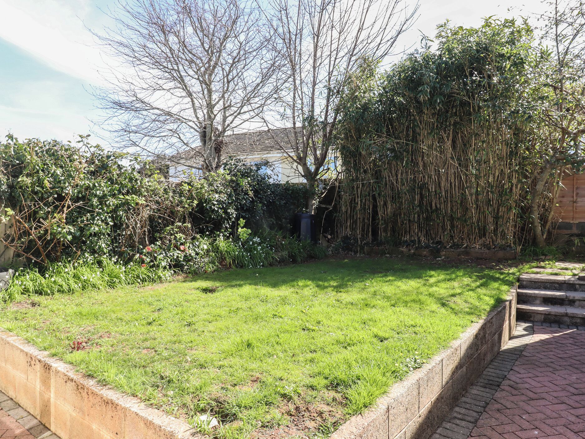 A well-maintained garden with a grassy lawn, dense shrubbery, and a variety of trees.