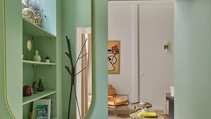 A room with a green wall, a round mirror, a bookshelf, a chair, and a small table with books. - Charming apartment St Germain des Près (Paris)