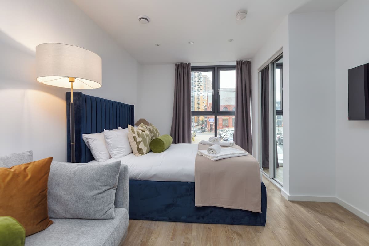 Camera d'albergo moderna con un letto, un divano, una lampada e un'ampia finestra con vista sulla città.