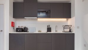 A modern kitchen with dark cabinets, a microwave, a coffee maker, and a sink. - Cable Street Serviced Apartments (Manchester)