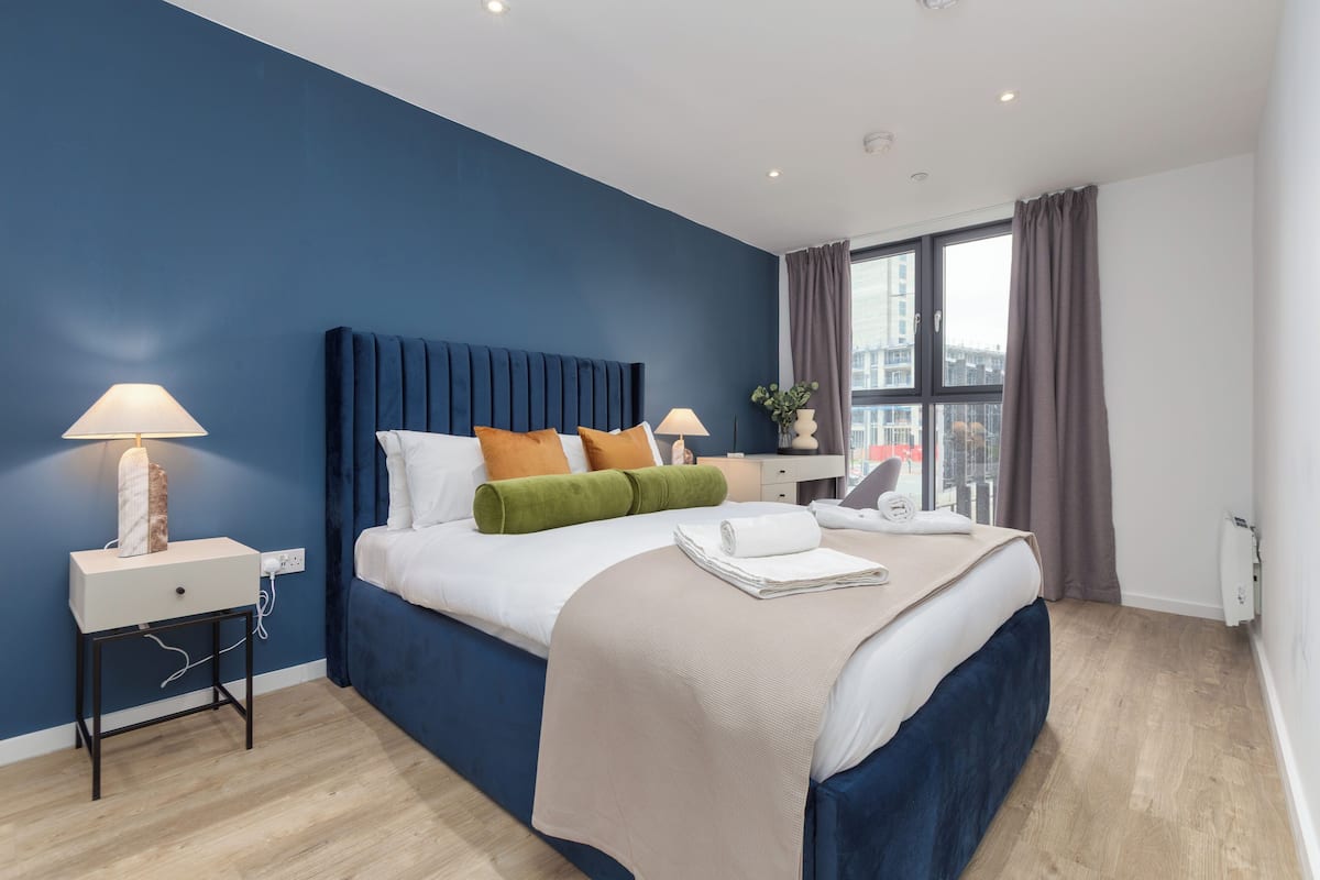 Una camera d'albergo moderna con un letto grande, un comodino, una scrivania e una finestra con tende.