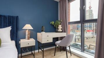Een moderne hotelkamer met een bed, een bureau, een stoel, een lamp en een groot raam met uitzicht op de stad.