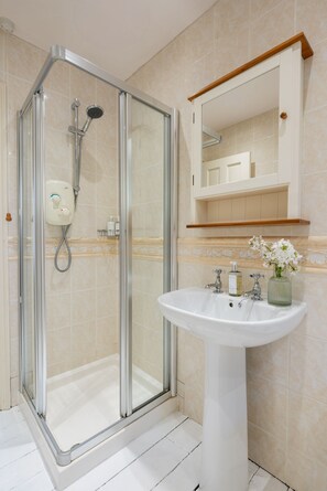 A modern bathroom with a glass-enclosed shower, a pedestal sink, and a mirror above the sink.