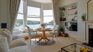 A living room with a bay window overlooking a body of water, a fireplace, and a television.