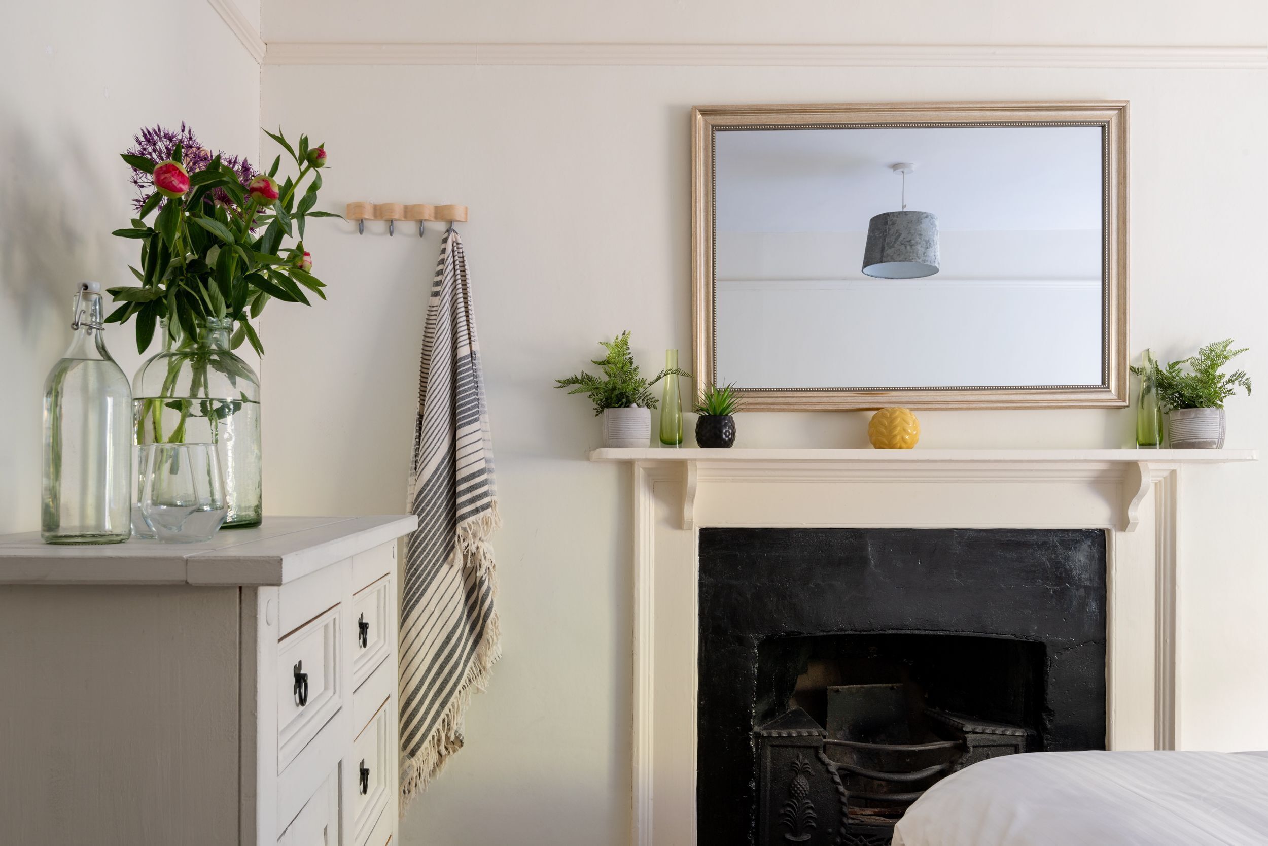 A bedroom with a white dresser, a framed picture above a fireplace, and a bed with white bedding.